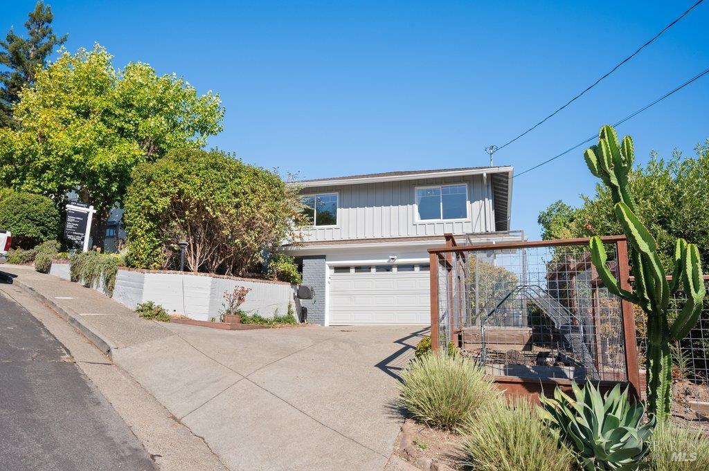 Two-story gray home with a white garage door, sloped driveway, metal gate, and cactus landscaping.