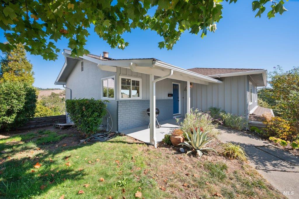 Single-story gray home with a blue front door and covered entry beneath leafy branches.