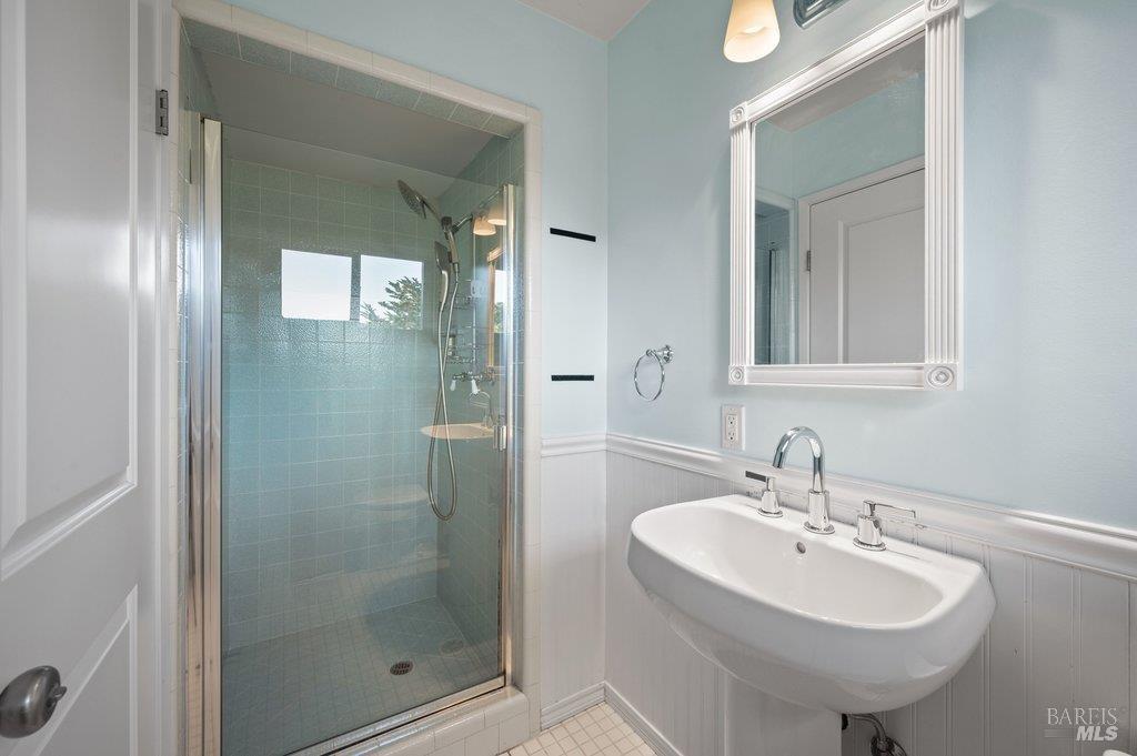 Bathroom with a blue-green tiled glass shower and white pedestal sink.
