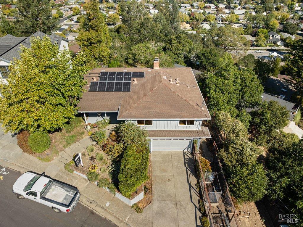 Aerial view of a tree-surrounded two-story home with rooftop solar panels and a driveway.