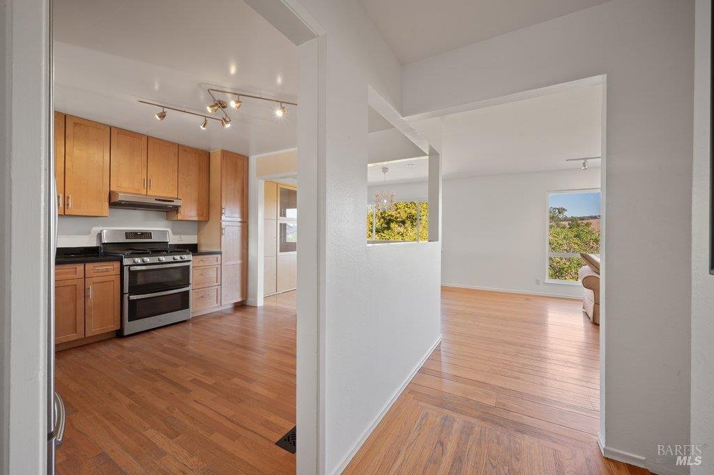 Kitchen with wood cabinets and stainless range opening to a bright room with hardwood floors.
