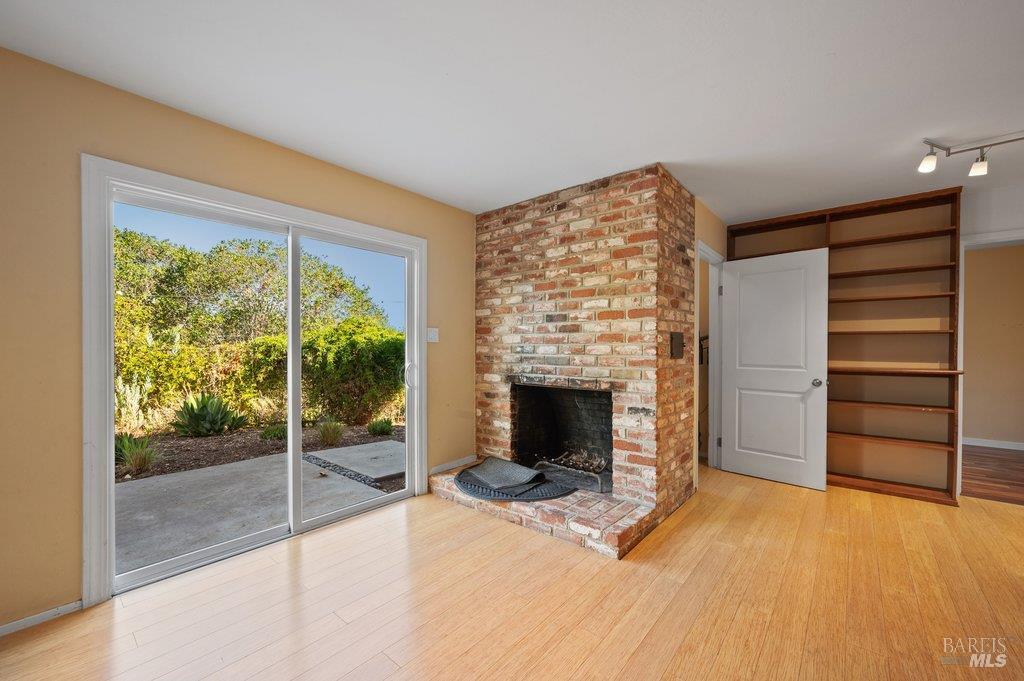 Empty living room with a brick fireplace, built-in shelves, and sliding glass doors to a patio.