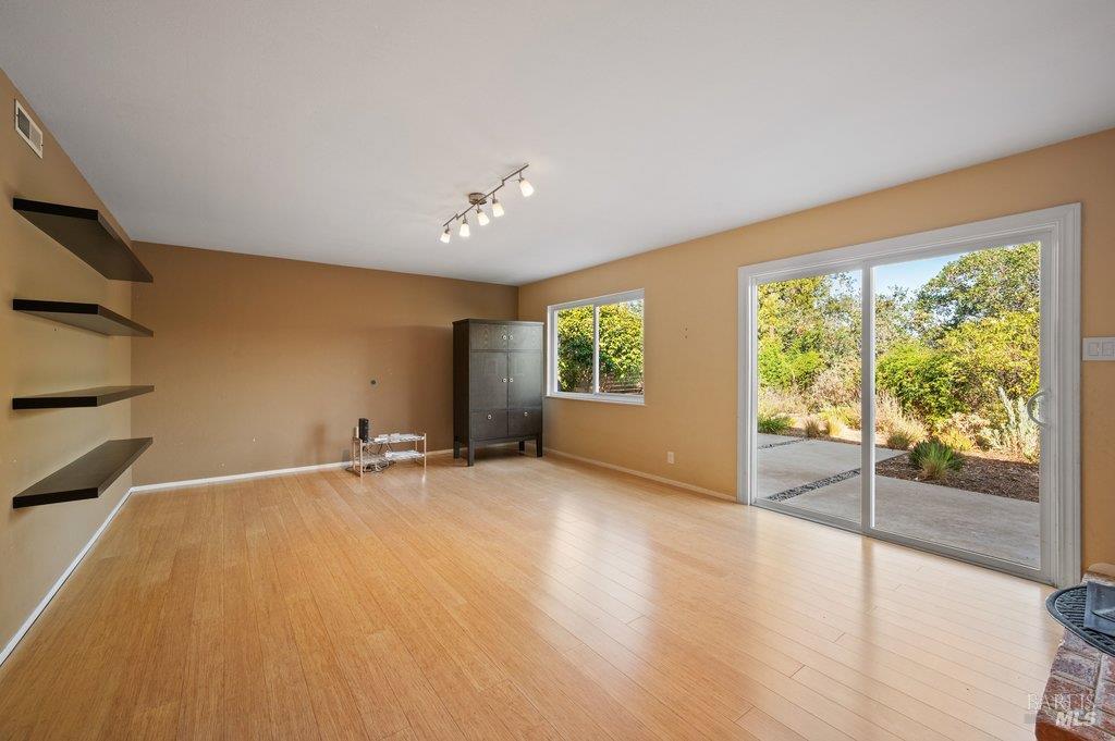 Living room with light wood floors, floating shelves, and a sliding glass door to the patio.