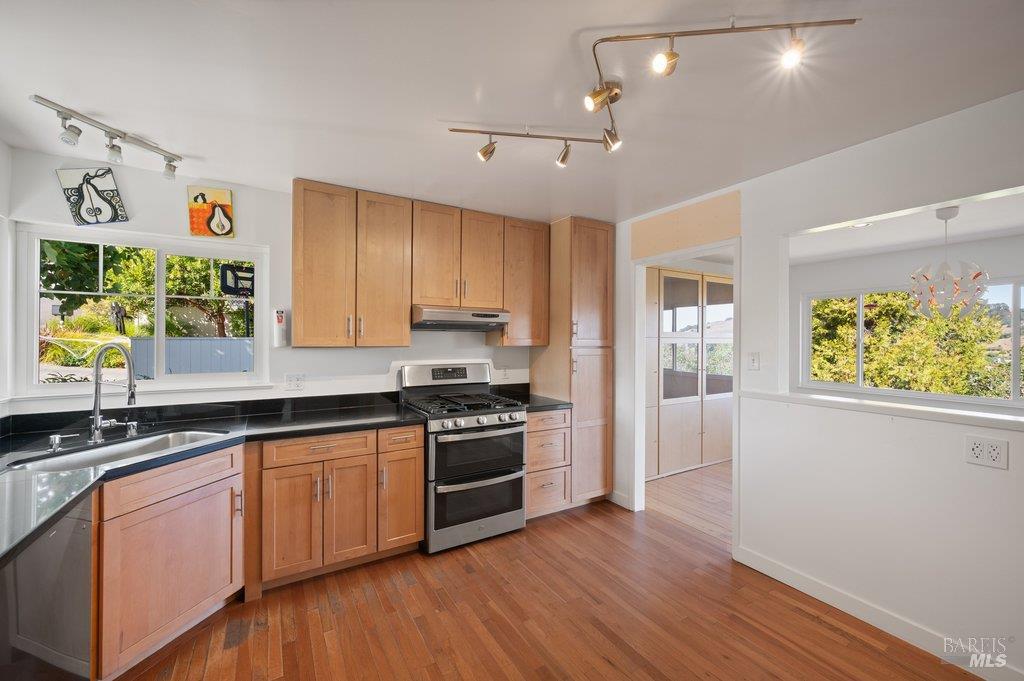 Kitchen with wood cabinets, black countertops, stainless steel range, and windows overlooking greenery.