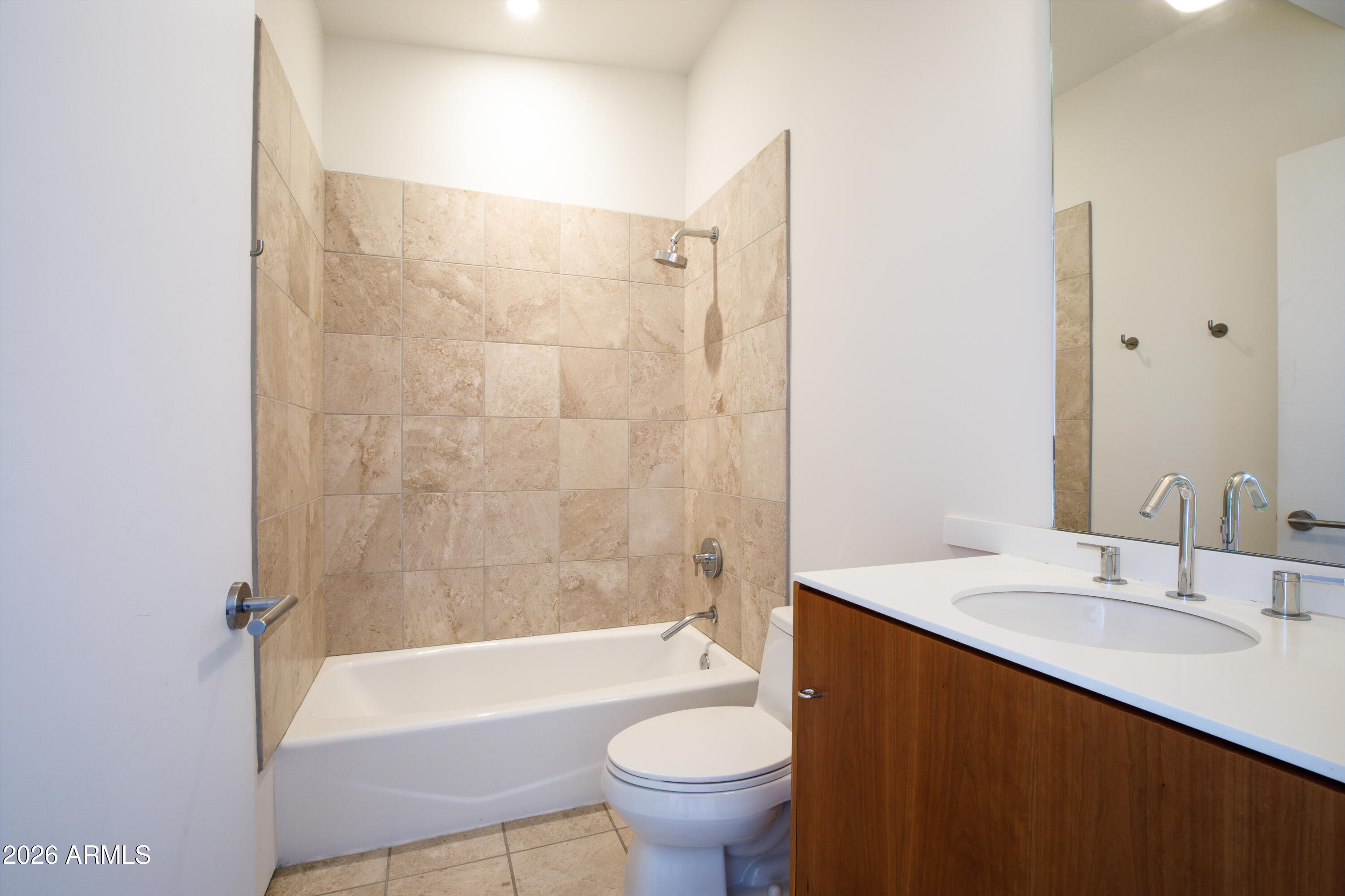 Bathroom with a beige tiled tub and shower beside a wood vanity and large mirror.