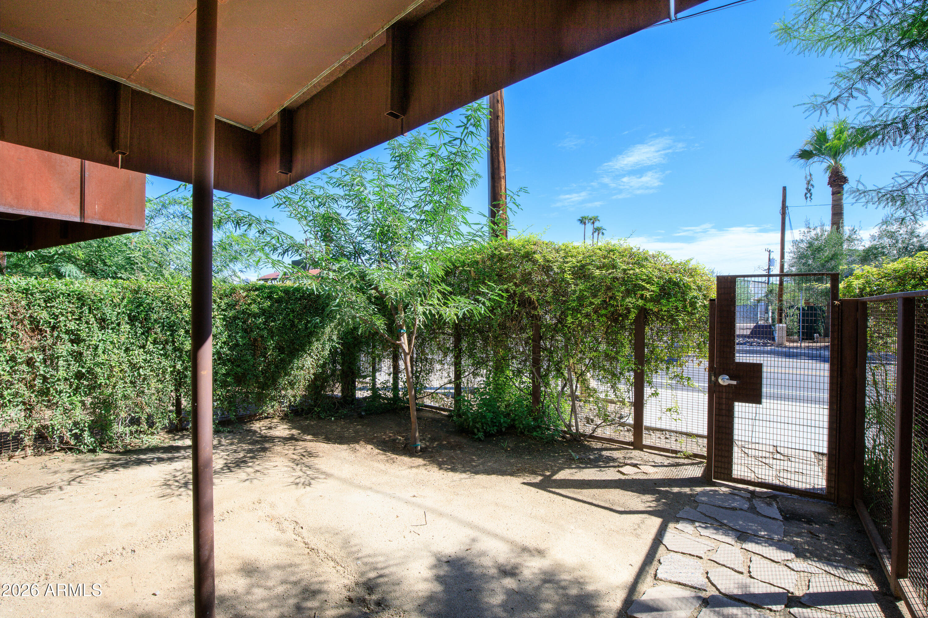 Enclosed courtyard with tall hedges, a mesh gate, sandy ground and stone pavers.