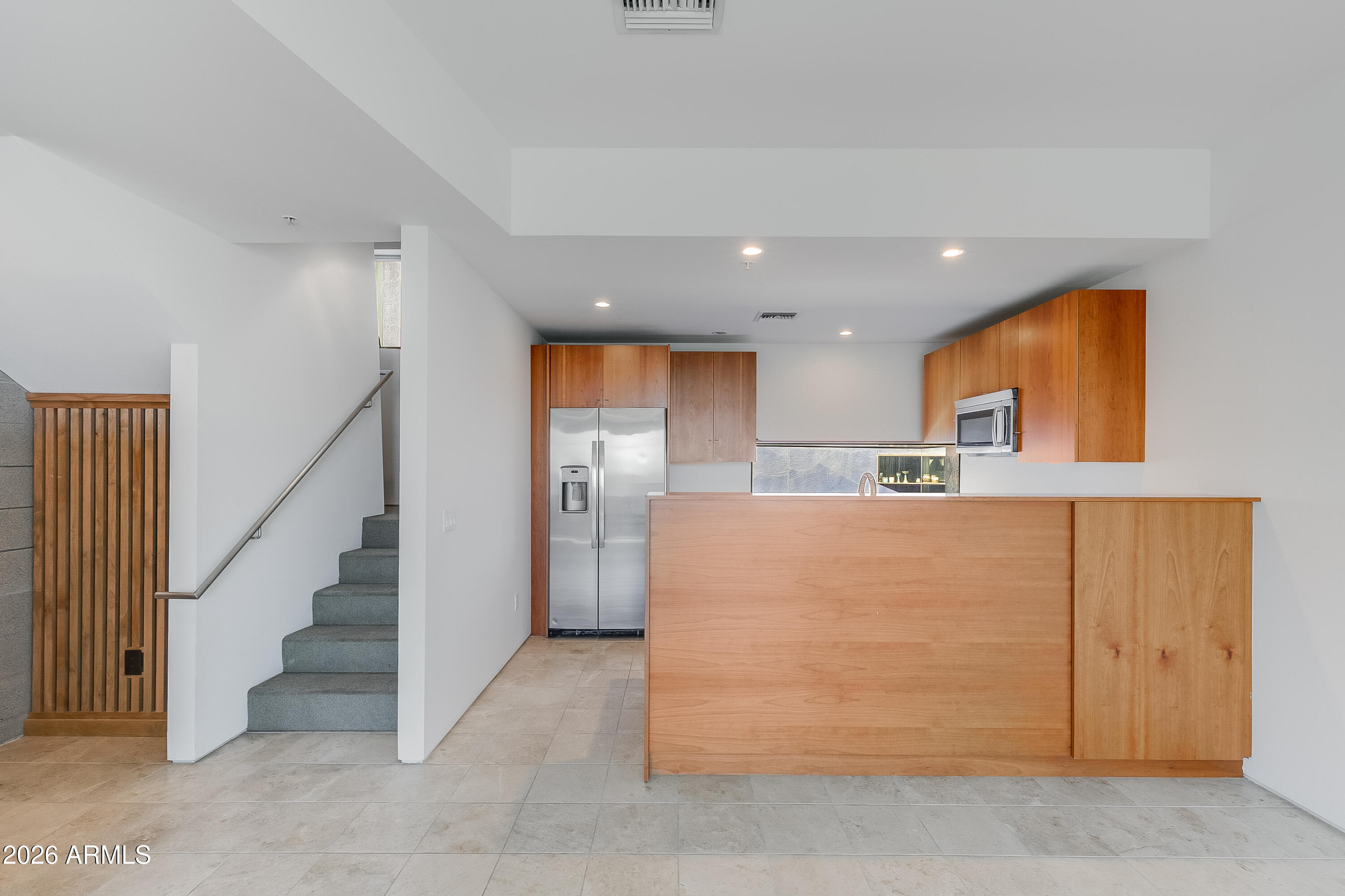 Kitchen with wood cabinetry, stainless appliances, and a broad breakfast bar beside the stairway.