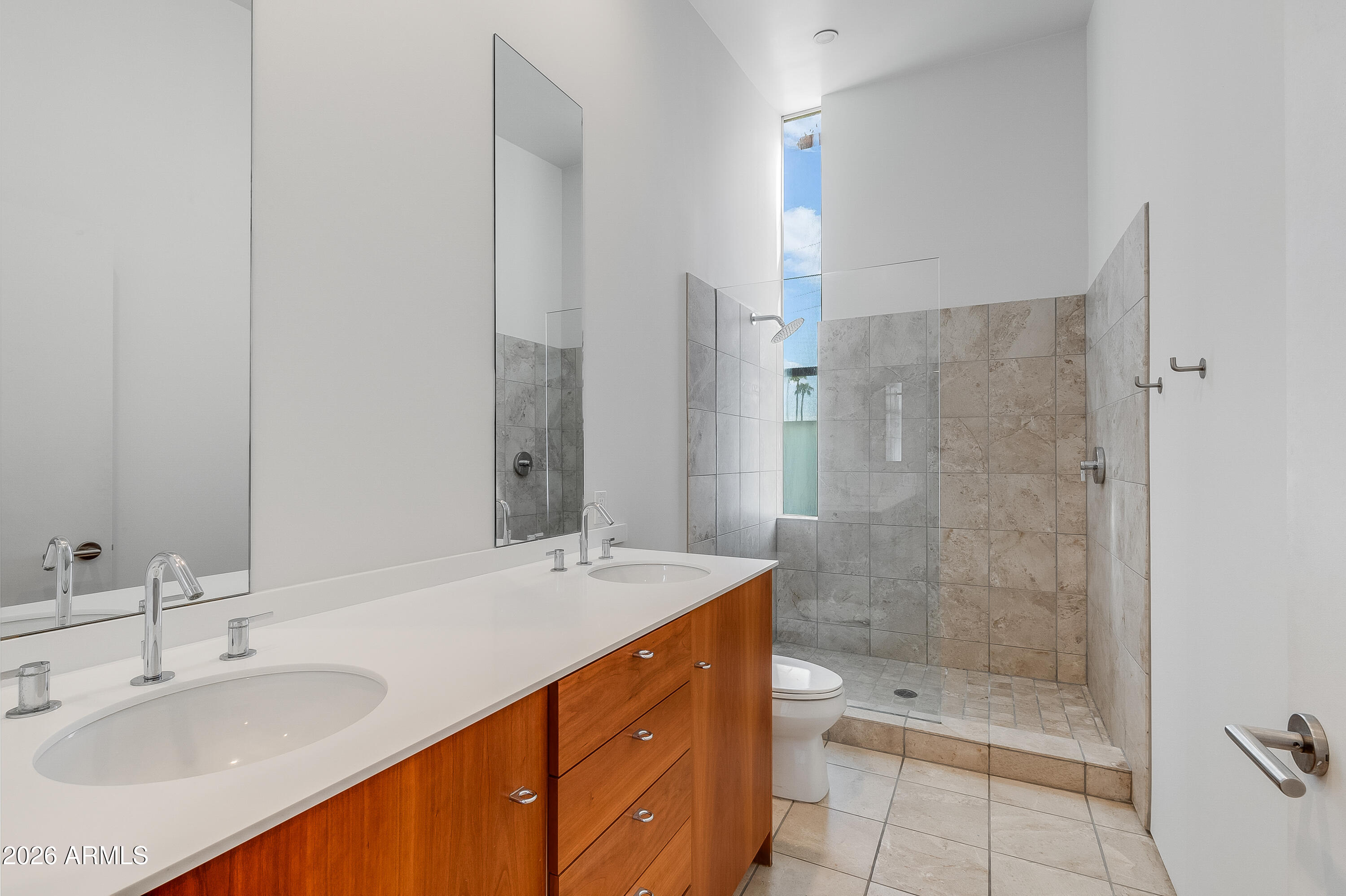 Bathroom with a double-sink vanity, warm wood cabinetry, and a glass-enclosed tiled shower.