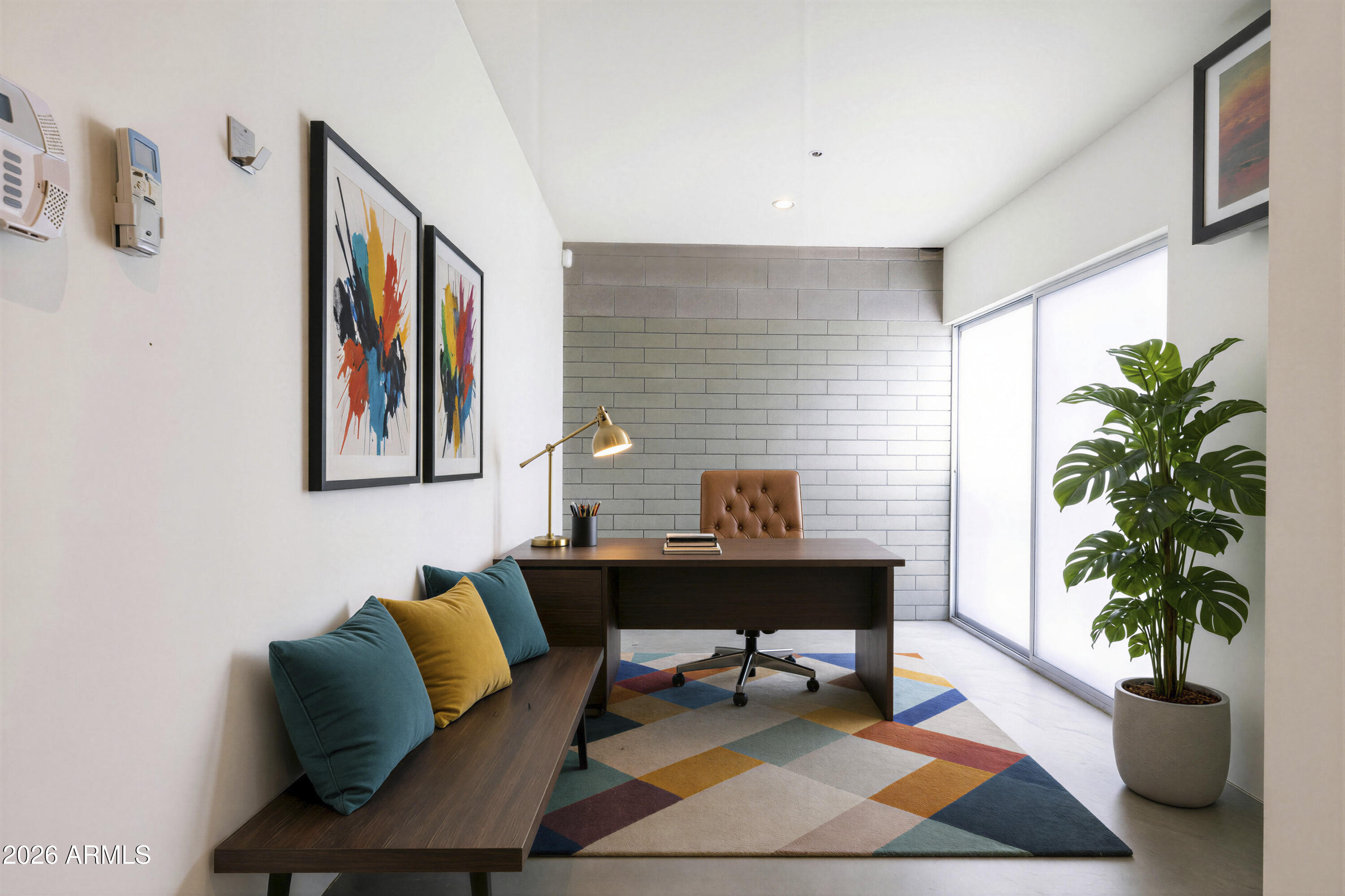 Furnished home office with a dark wood desk, colorful rug, and potted monstera beside sliding glass doors.