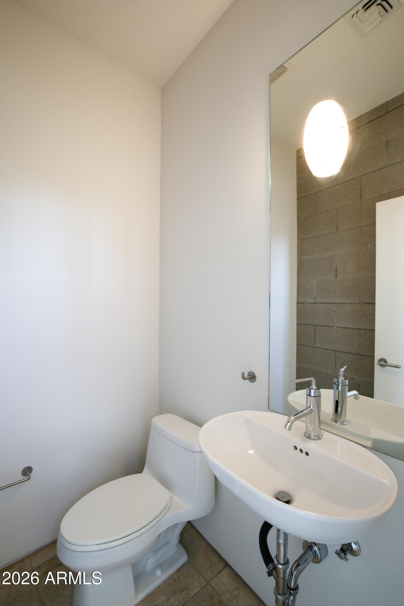 Compact bathroom with a white toilet, oval sink, large mirror, and gray block-tile accent wall.