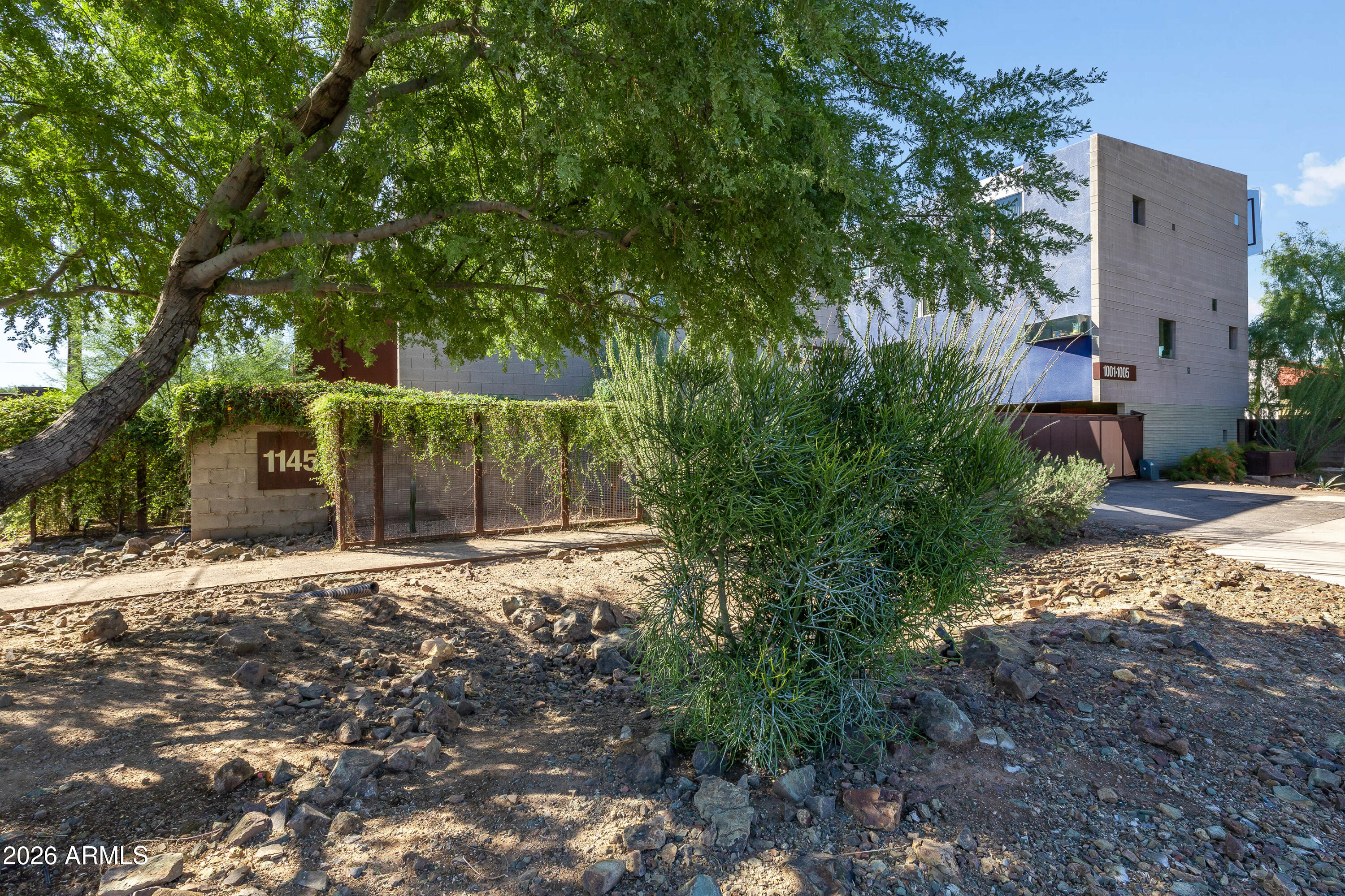 Modern multi-unit building entrance with a gated driveway, desert landscaping, and address marker 1145.