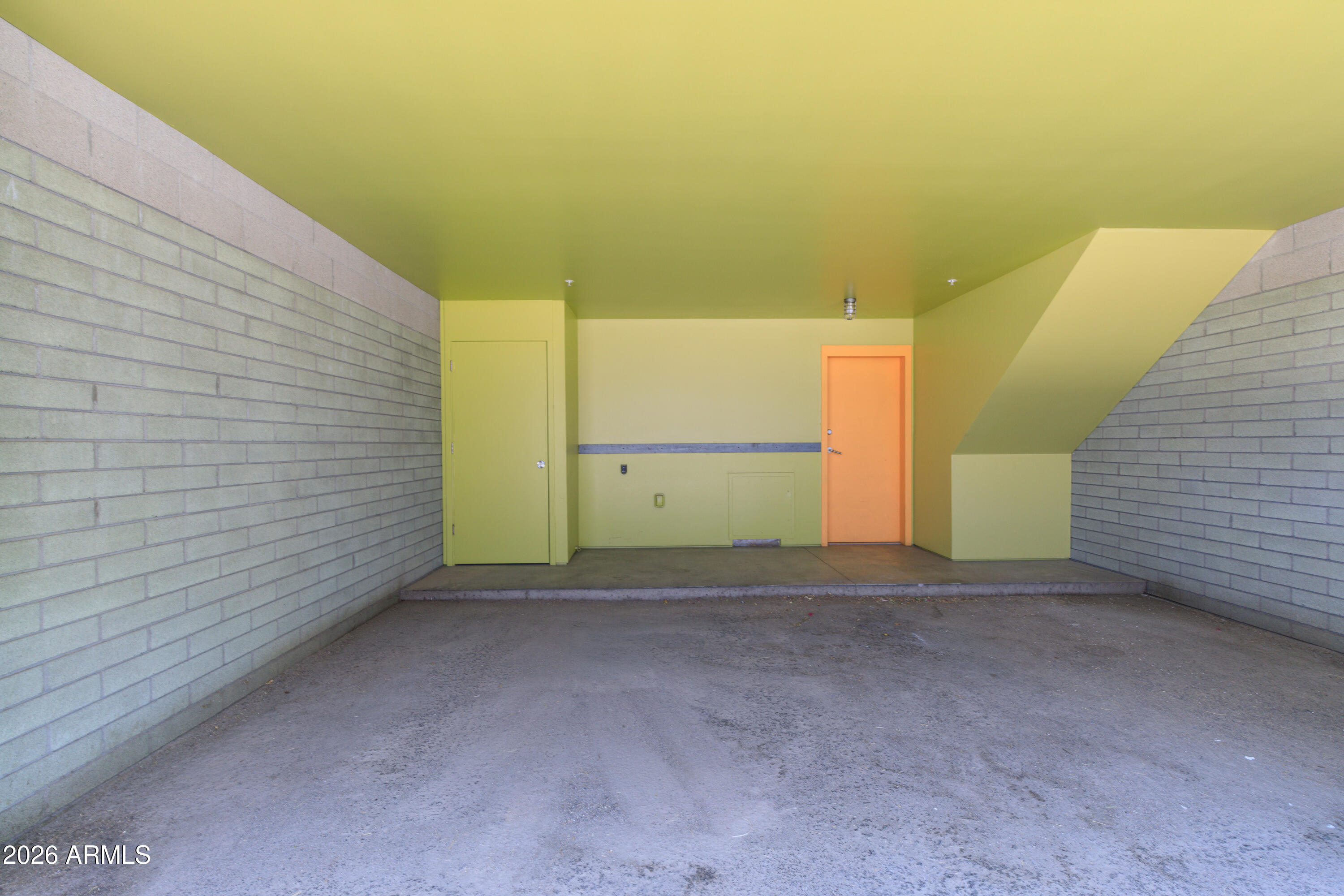 Covered parking bay with gray block walls, concrete floor, and an orange door.