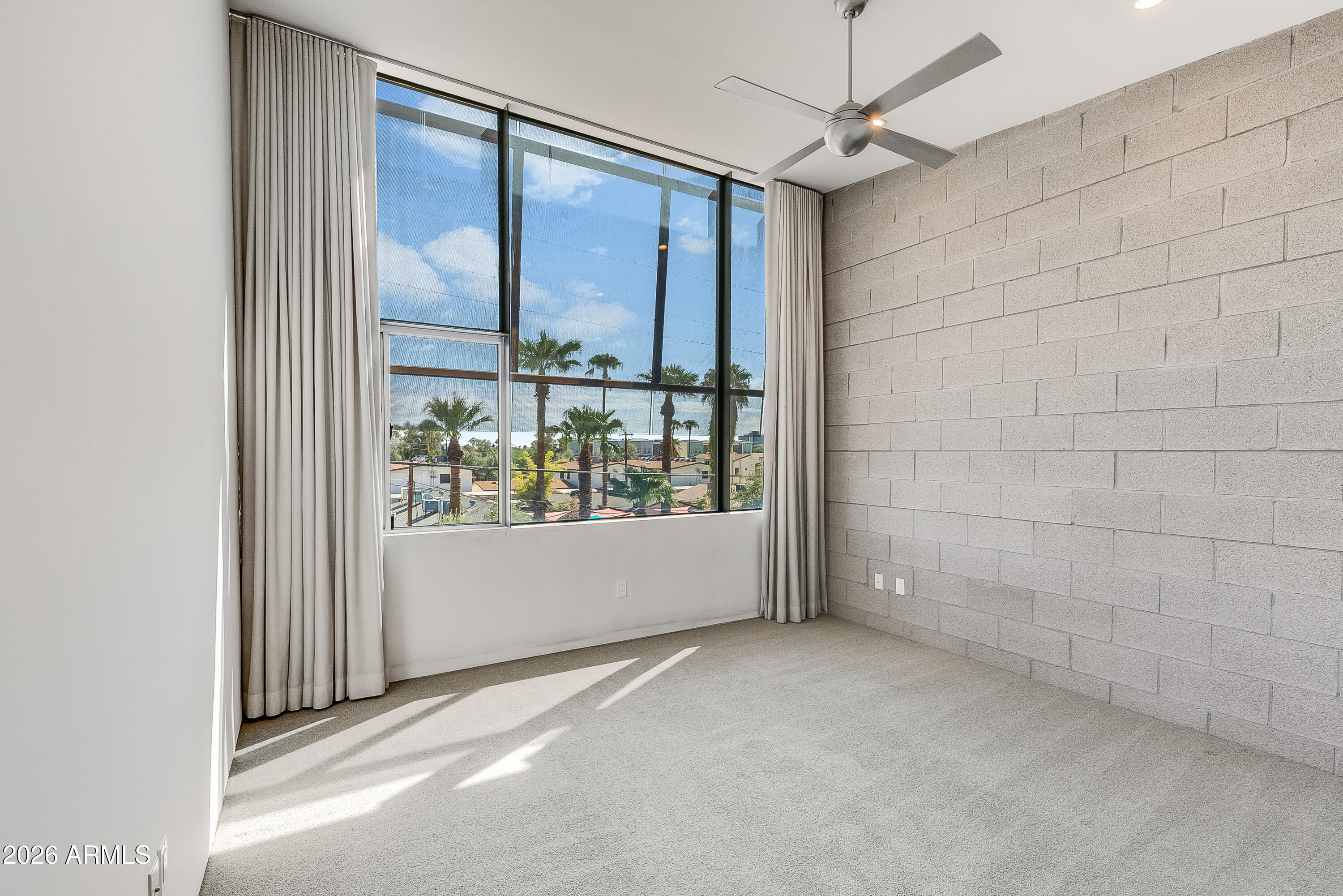 Vacant room with a large curtained window, exposed block wall, and ceiling fan.
