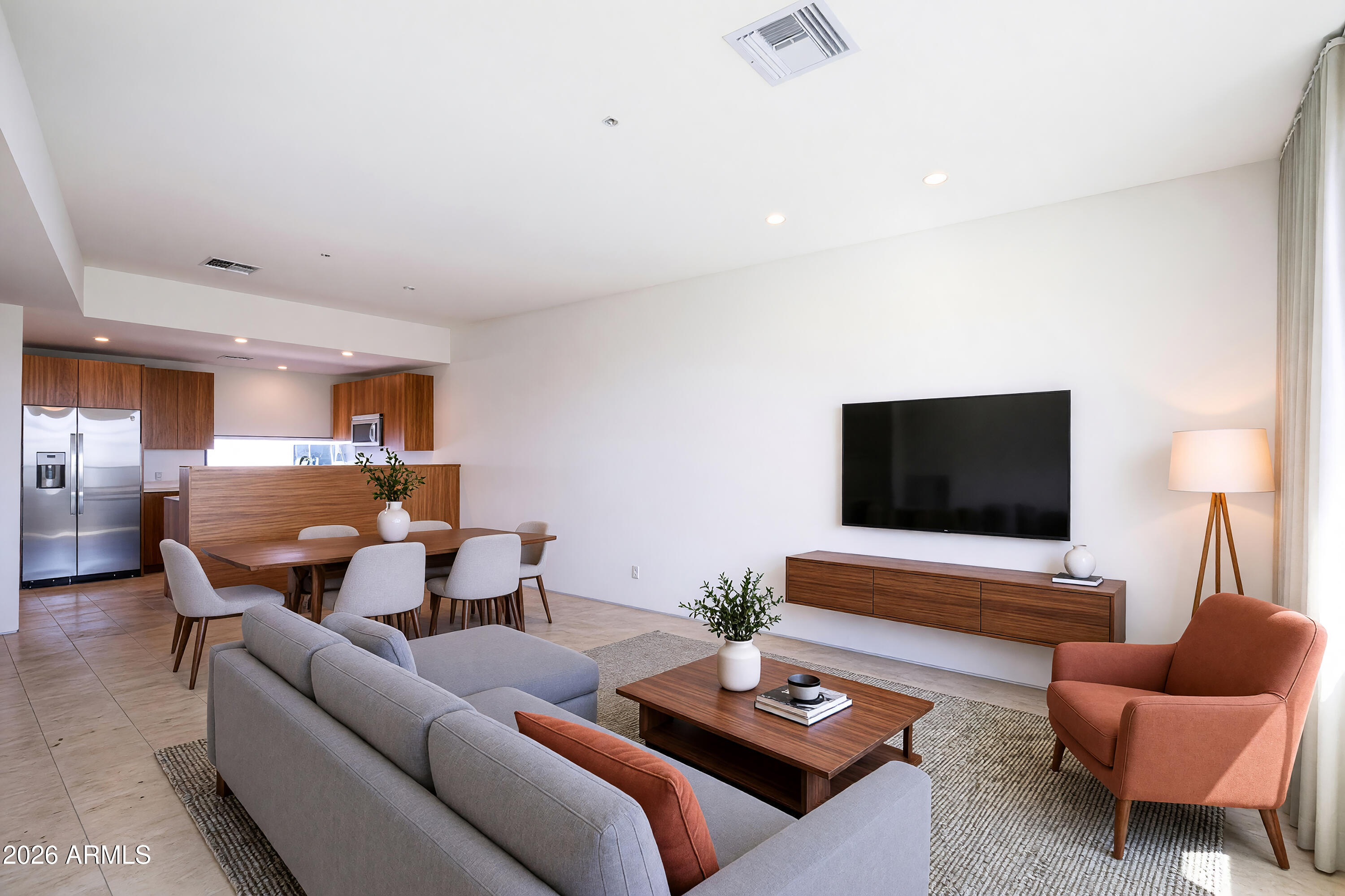 Open-plan living room with gray sectional, rust-colored chair, wood coffee table, and adjoining kitchen.