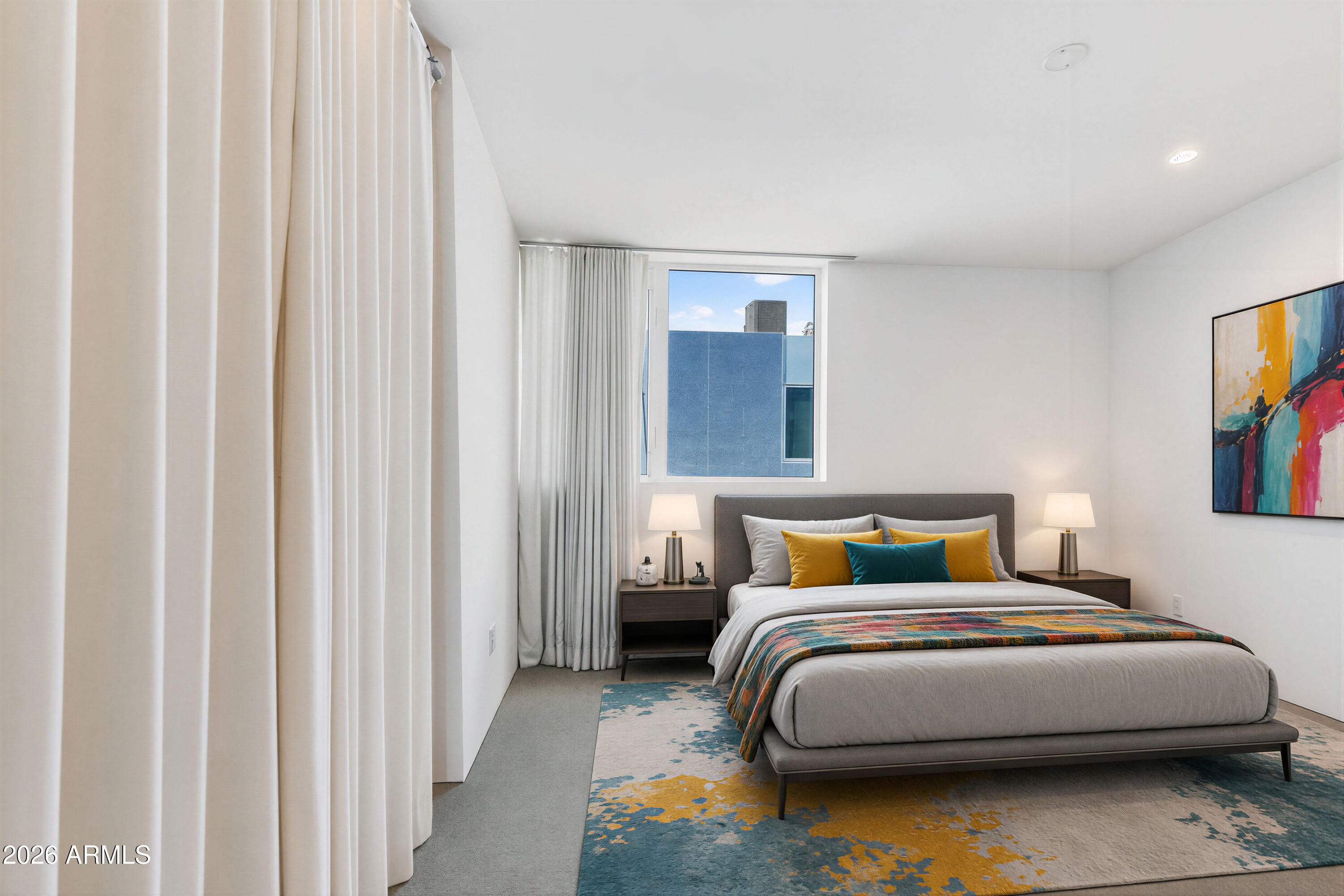 Modern bedroom with a gray bed, colorful accent pillows, abstract artwork, and a patterned area rug.