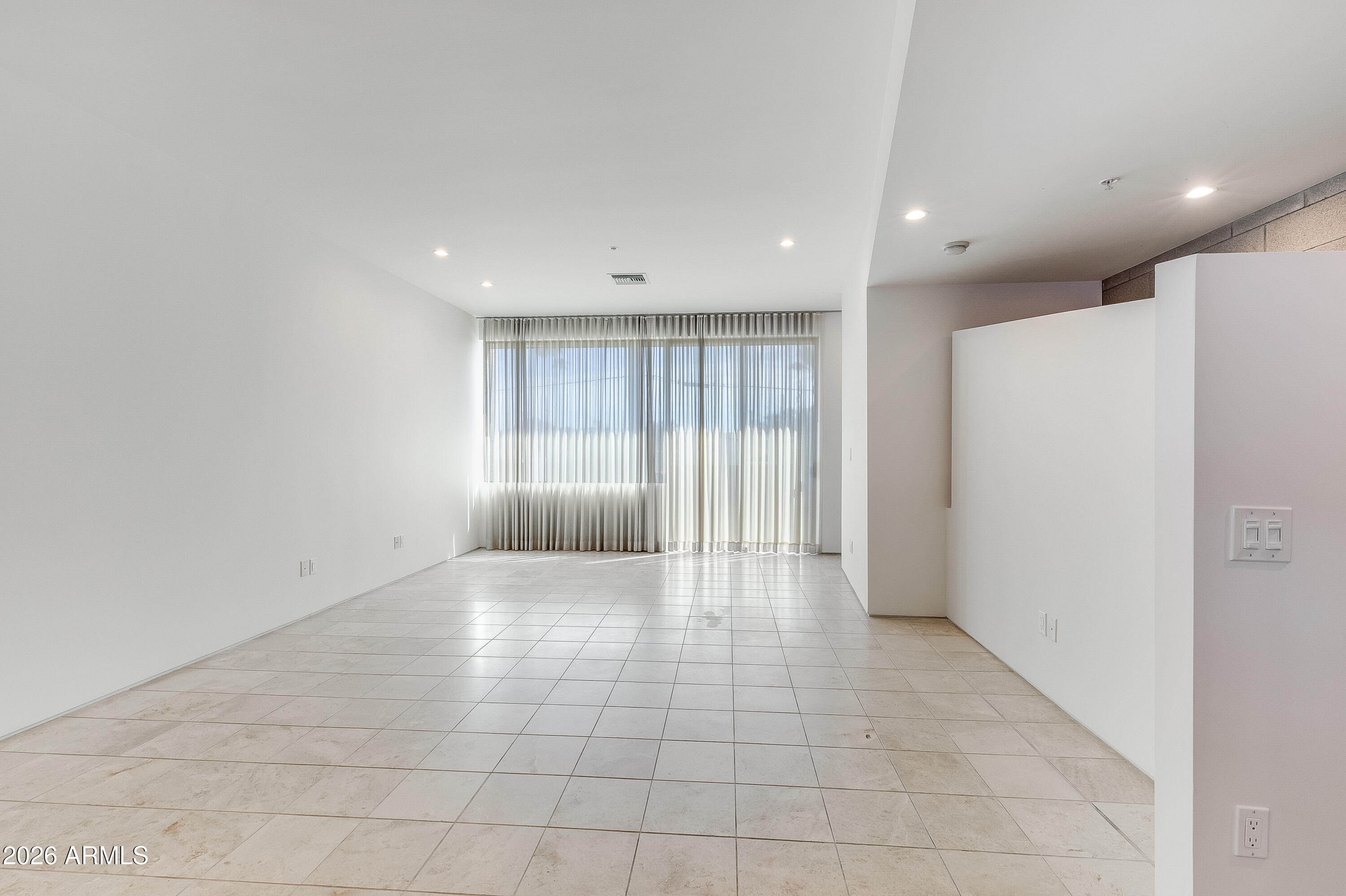 Vacant living room with tiled floors and large curtained windows.
