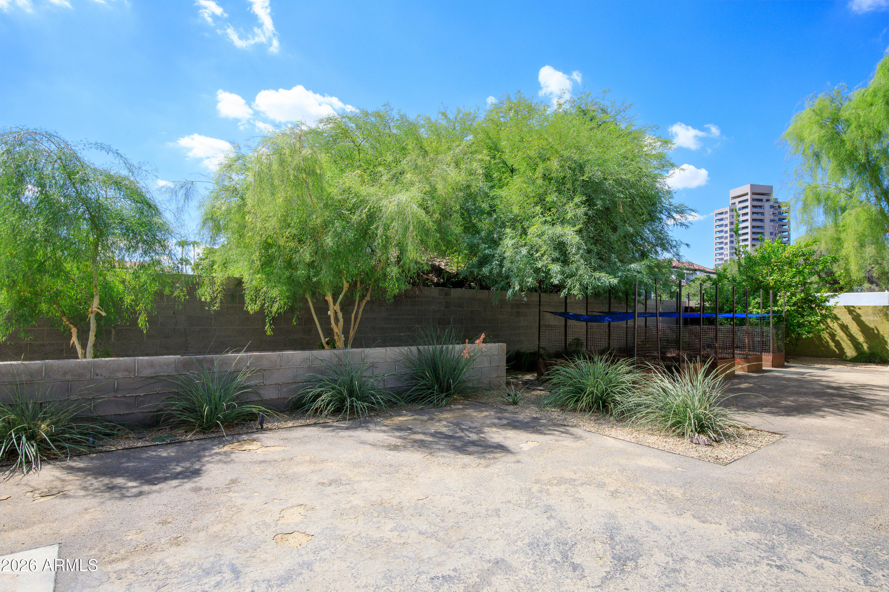 Landscaped grounds with mature trees and a fenced blue-canopy structure beside a high-rise building.