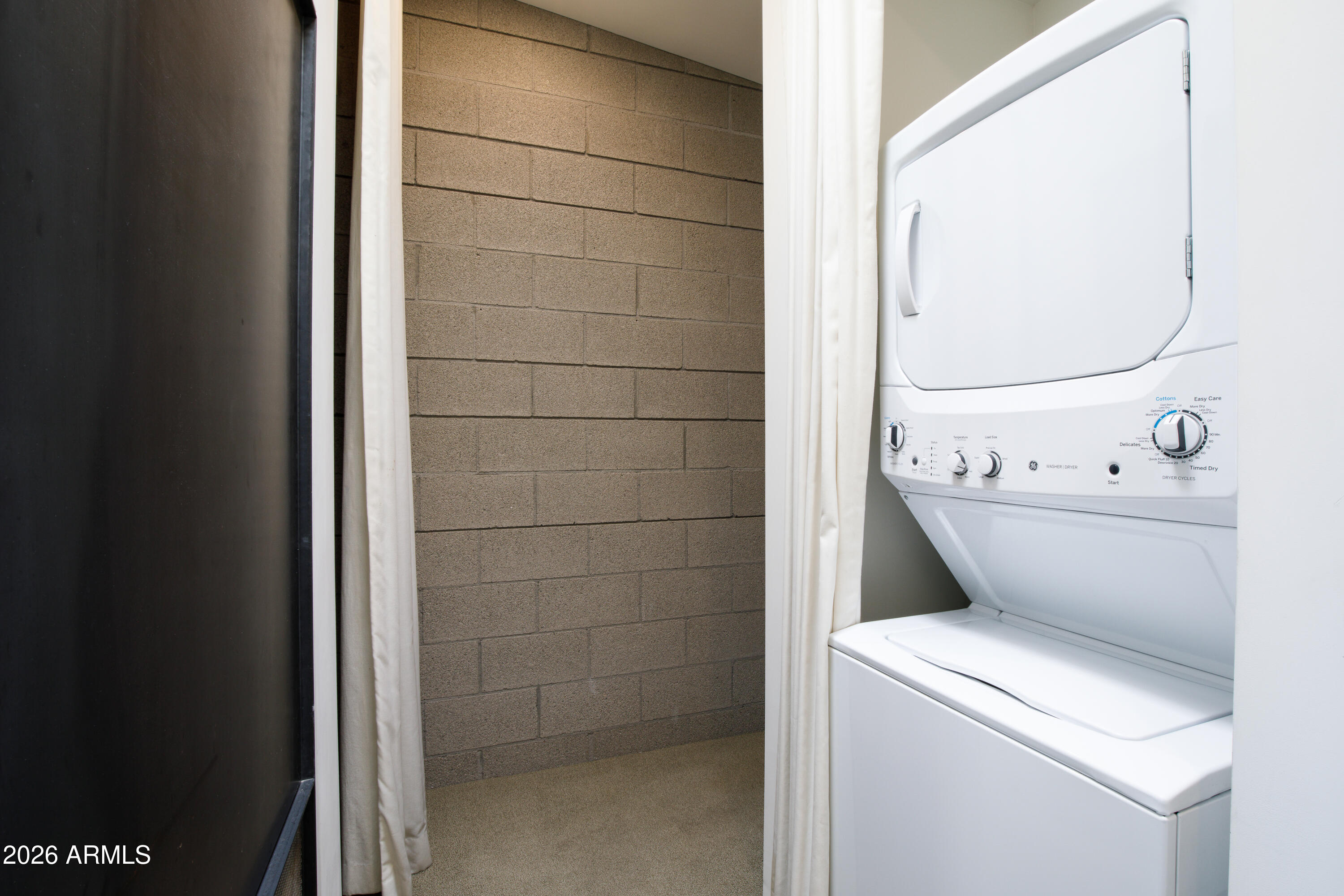 Laundry area with a white stacked washer and dryer beside a tan concrete block wall.