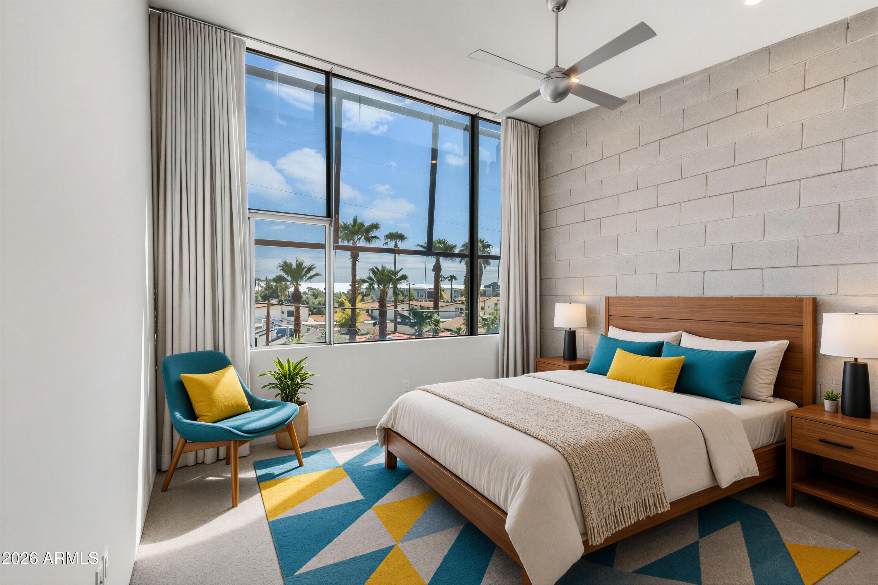Staged bedroom with a large palm-framed window, wood bed, and colorful geometric rug.