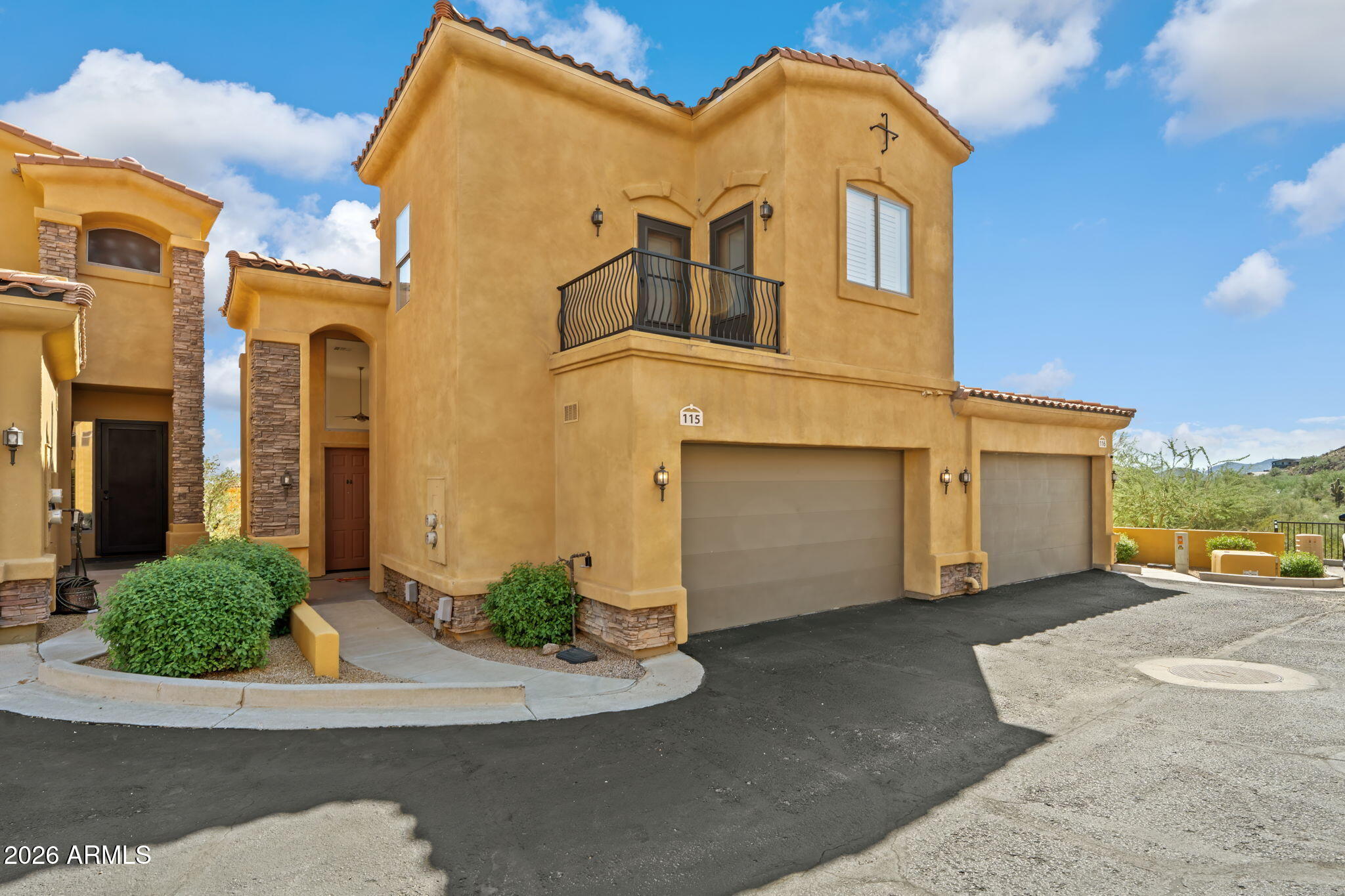 Two-story tan stucco townhouse with a black balcony, tiled roof, and attached garages.