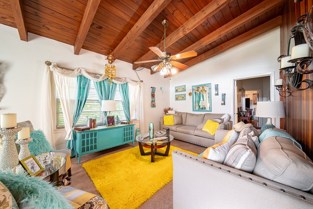 Living room with exposed wood ceiling beams, beige sofas, yellow rug, and teal console.