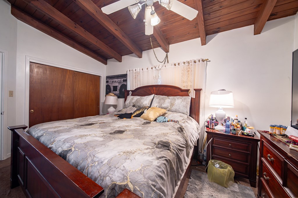Bedroom with a large bed beneath an exposed-beam wood ceiling and ceiling fan.