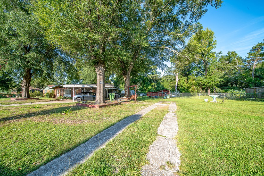 Grassy yard with a concrete walkway, mature trees, small outbuildings, and a chain-link fence.