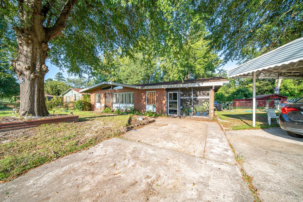 Single-story brick home with a wide driveway, covered carport, and large shade tree.