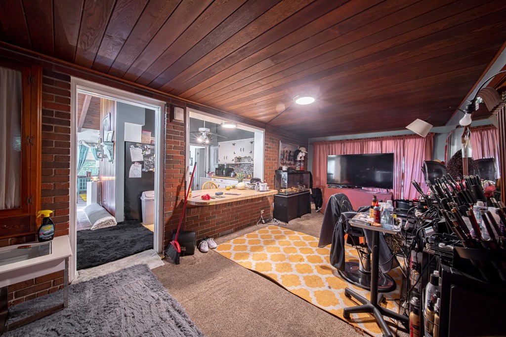 Living room with a wood-plank ceiling, brick walls, and a kitchen pass-through.