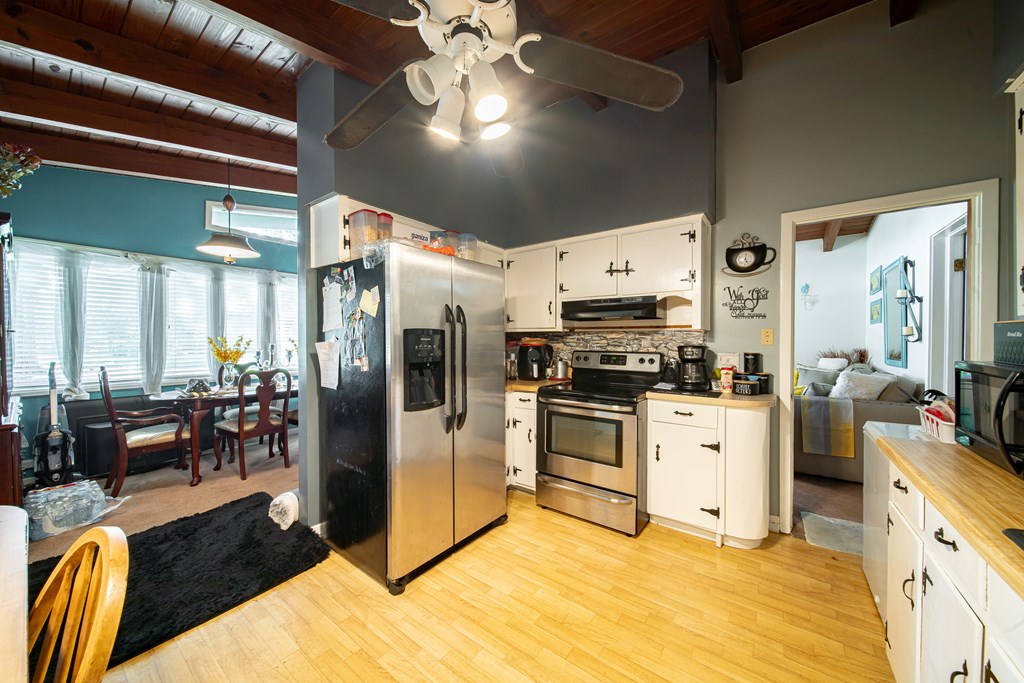 Kitchen with white cabinets, stainless steel appliances, and an adjoining dining area beneath a wood ceiling.