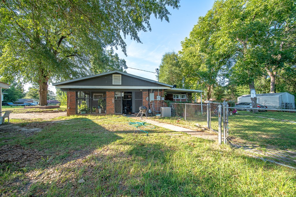 Rear of a single-story brick house with a fenced grassy yard and mature shade trees.