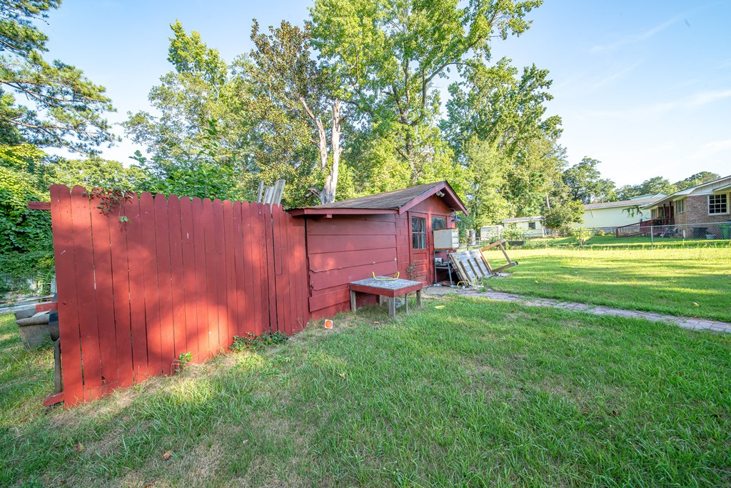 Backyard with a red shed and matching fence beside a grassy lawn and mature trees.