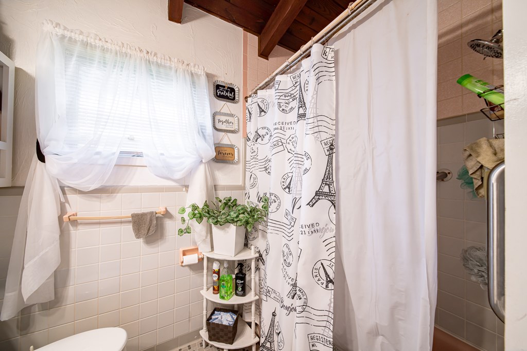 Bathroom with Paris-print shower curtain, tiled walls, curtained window, and exposed wood ceiling.