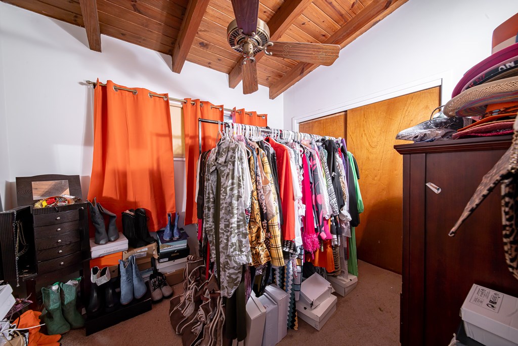 Walk-in closet with clothing racks, shoe storage, orange curtains, and a wood-plank ceiling.