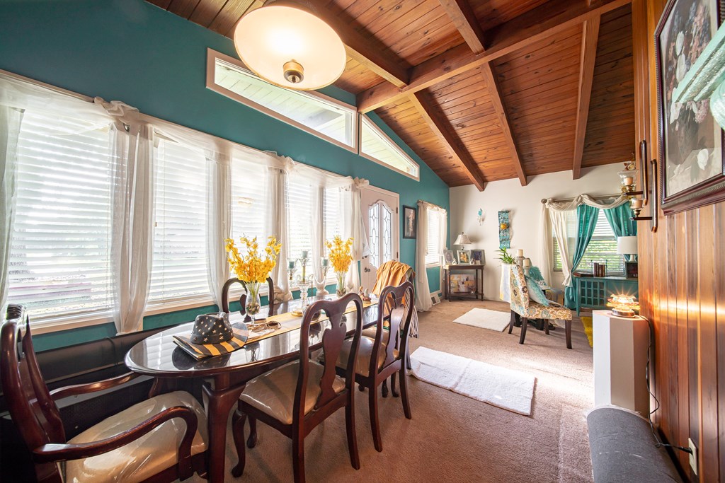 Dining and living area with a vaulted wood ceiling, teal walls, and a dark dining table by large windows.