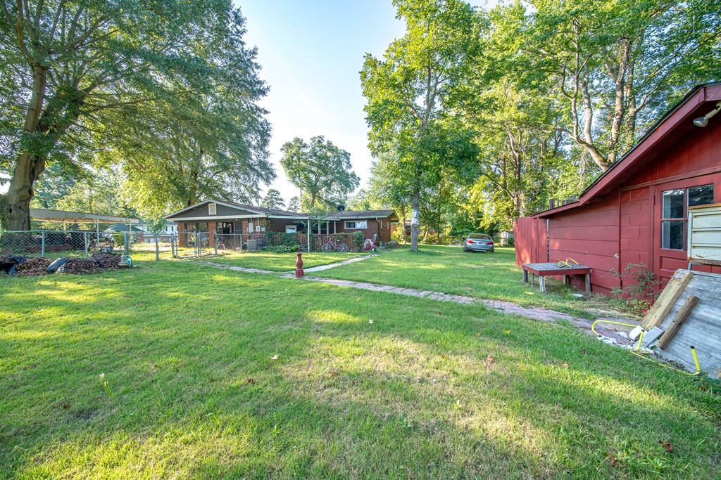 Grassy yard with mature trees, a red outbuilding, and a single-story house in the background.