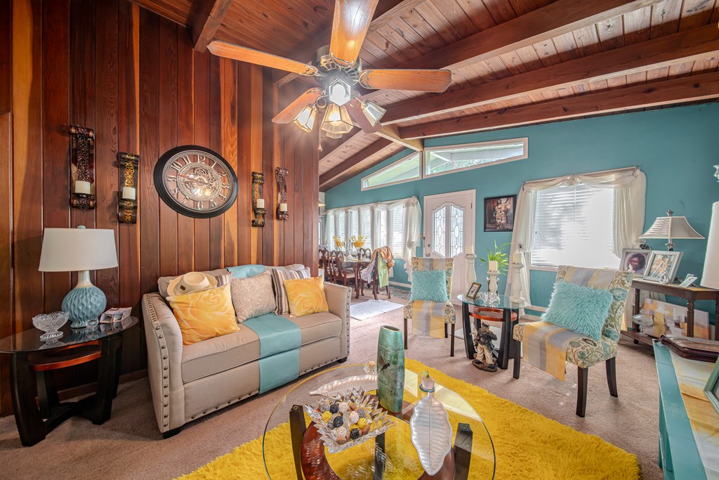 Furnished living room with a vaulted wood ceiling, wood-paneled walls, and teal accents.