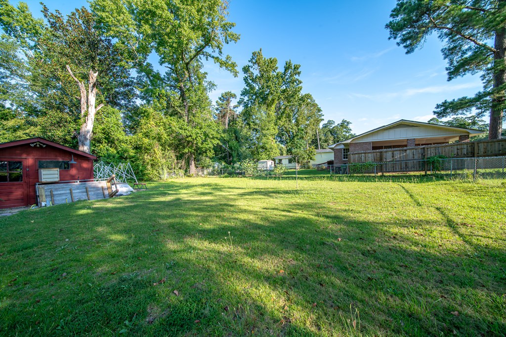 Grassy backyard with a red shed, fenced homes, and mature trees.