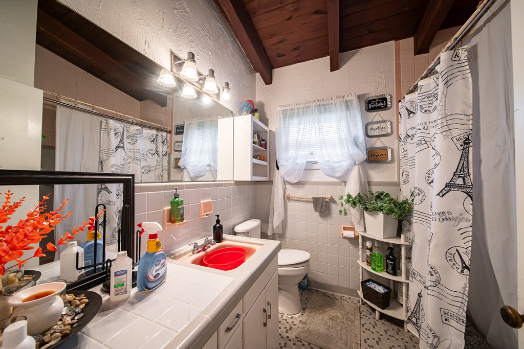 Bathroom with a red sink, Paris-themed shower curtain, and exposed wood ceiling beams.