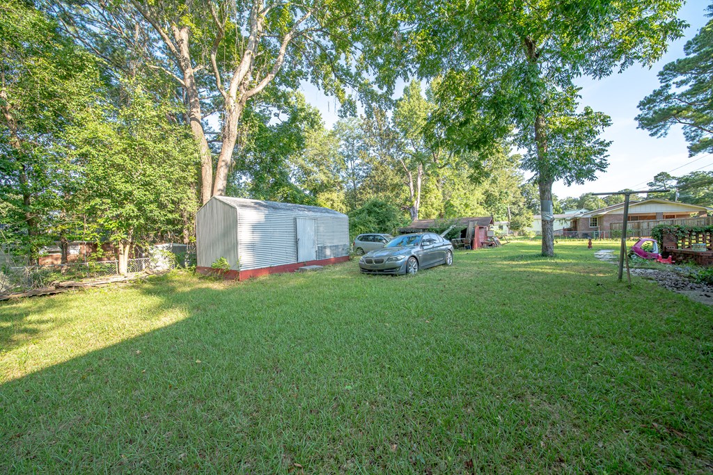 Grassy property yard with a metal shed, parked cars, mature trees, and a house.