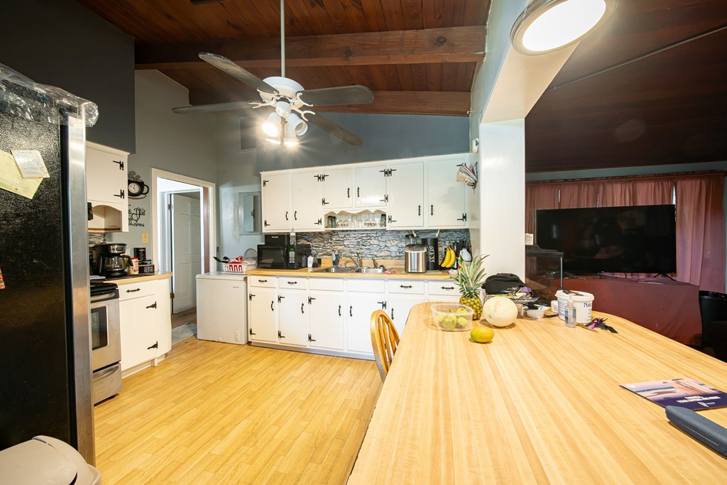 Kitchen with white cabinets, stone backsplash, large dining table, and exposed wood ceiling.