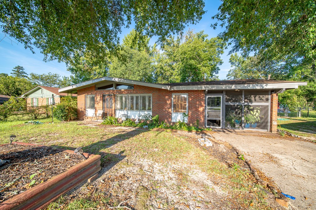 Single-story brick house with a screened porch, concrete driveway, and mature trees.