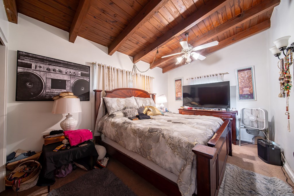 Bedroom with a large wooden bed beneath a vaulted ceiling with exposed wood beams.