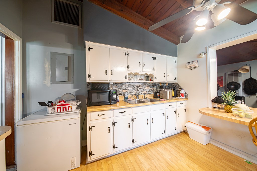 Kitchen with white cabinets, a stone-pattern backsplash, and a vaulted wood ceiling with a ceiling fan.