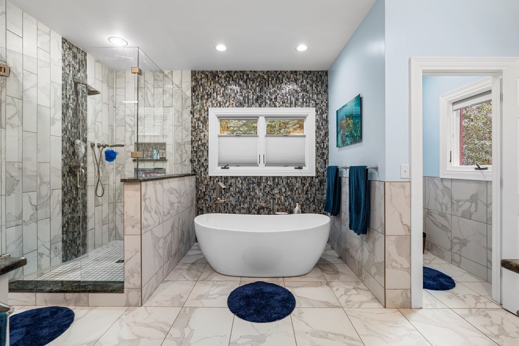 Bathroom with a freestanding tub, glass shower, and dark mosaic accent wall.
