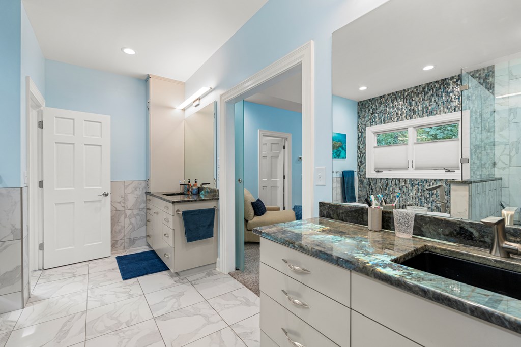 Bathroom with a long stone double-sink vanity and glass shower backed by blue mosaic tile.