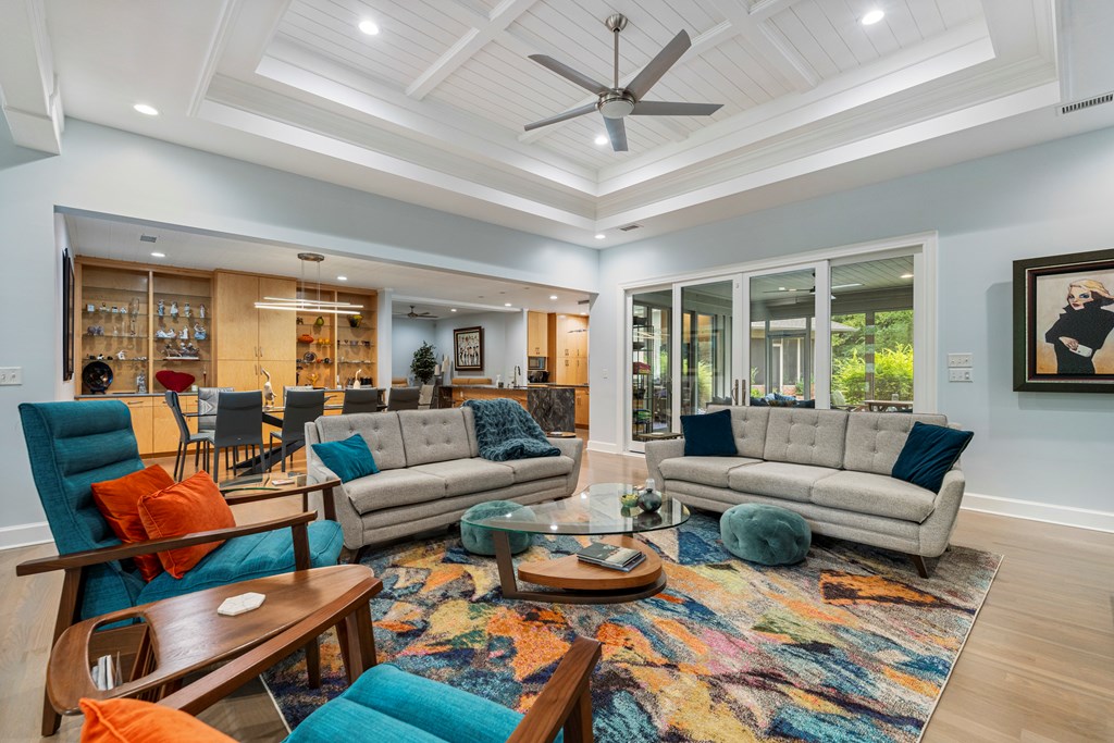 Living room with a tray ceiling, gray sofas, colorful rug, built-in cabinetry, and glass doors to greenery.