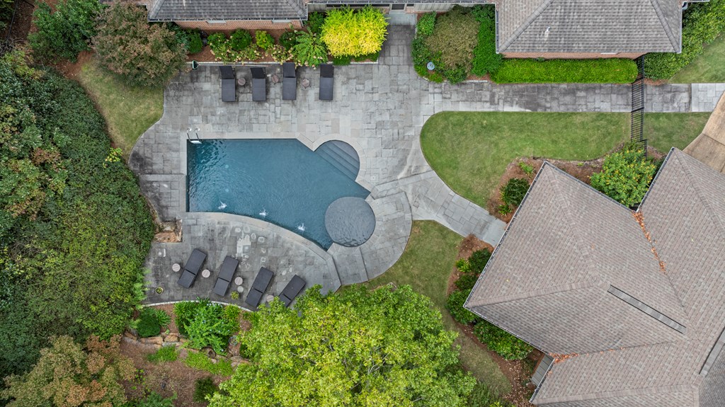 Aerial view of a backyard pool and circular spa surrounded by a stone patio and landscaped lawn.