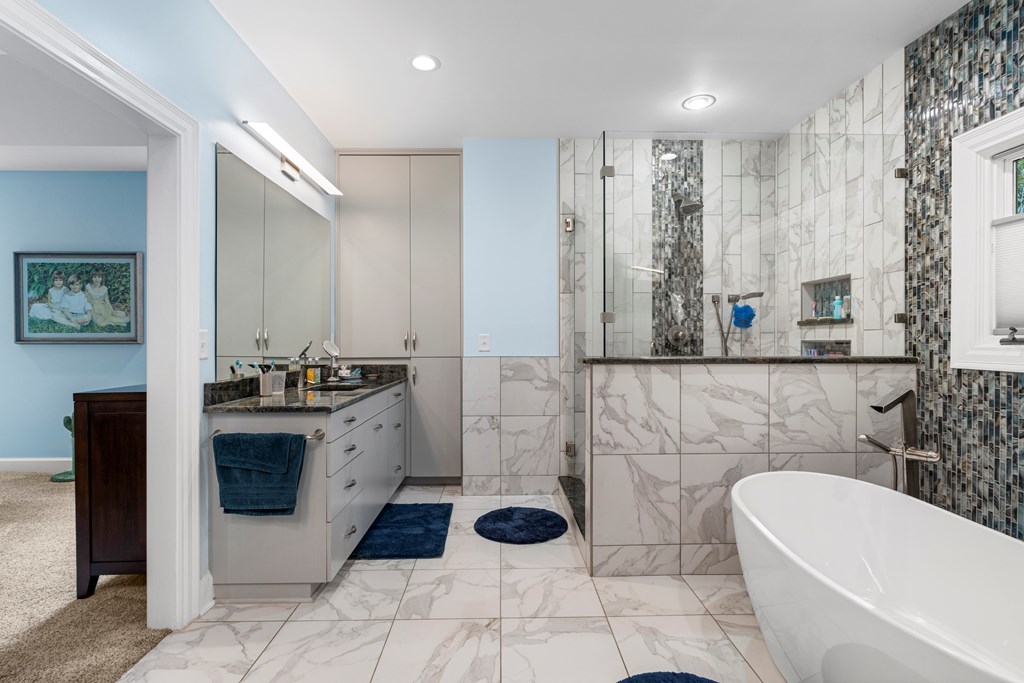 Bathroom with a marble-look tiled shower, double vanity, and freestanding soaking tub.