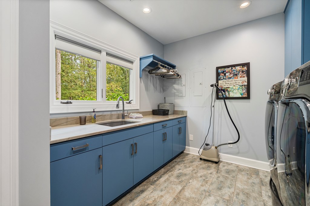 Laundry room with blue cabinets, a sink beneath two windows, and front-loading machines.